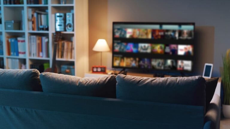 Salon de nuit avec un canapé au premier plan et une télévision affichant un menu de service de streaming Fast TV en arrière-plan.
